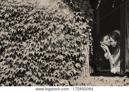 A Bkack And White Picture Of Bride And Groom Daydreaming In A Window Surrounded By Ivy