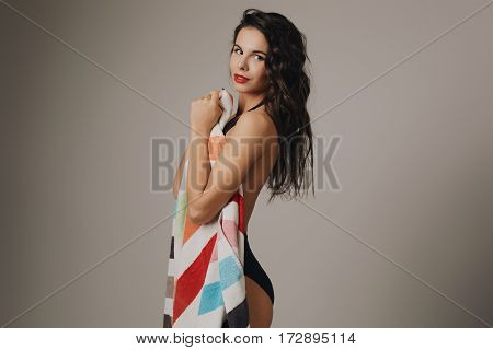 Fashion photo of beautiful and young lady in swimsuits posing in studio, holding colorful towel