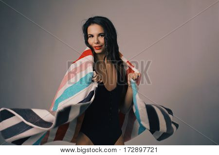 Fashion photo of beautiful and young lady in swimsuits posing in studio, holding colorful towel