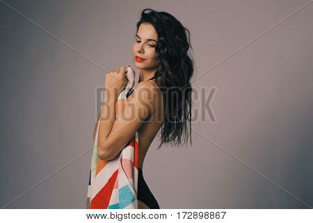 Fashion photo of beautiful and young lady in swimsuits posing in studio, holding colorful towel