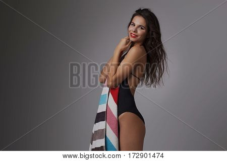 Fashion photo of beautiful and young lady in swimsuits posing in studio, holding colorful towel