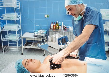 Male surgeon resuscitating an unconscious patient with a defibrillator at the hospital