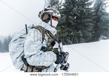 Winter arctic mountains warfare. Action in cold conditions. Trooper with weapons in forest somewhere above the Arctic Circle. Profile, side view