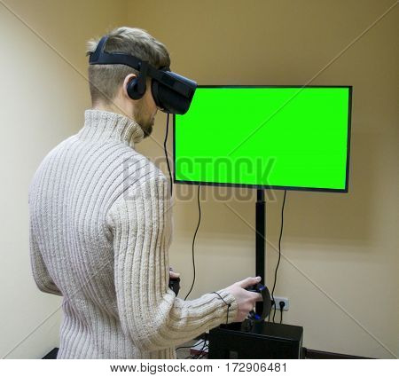 Man in helmet virtual reality plays game. Green screen. VR-headset display with headphones for virtual reality game in office. High-tech devices. Augmented reality device creating virtual space