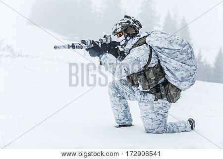 Winter arctic mountains warfare. Action in cold conditions. Trooper with weapons in forest somewhere above the Arctic Circle on the knee