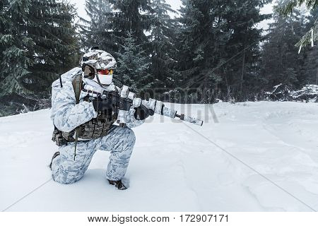 Winter arctic mountains warfare. Action in cold conditions. Trooper with weapons in forest somewhere above the Arctic Circle on one knee