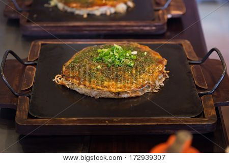 Close up of japanese local food called okonomiyaki or hiroshima pizza cooked by mixed cabbage pork noodle egg and sauce on iron plate in osaka Japan.