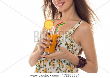 close up of cheerful brunette woman in sarafan with floral patter drinks fresh orange cocktail and smiling isolated on white