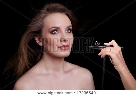 Beauty Fashion Model Woman portrait. Concept Girl face with perfect skin in dark Background with hand holding aerograph.