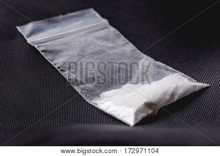 Cocaine in plastic packet on black background, macro closeup photo. Portion of drugs