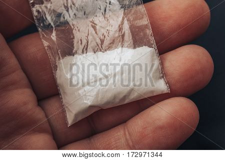 Plastic packet with cocaine powder or another drugs in mans hand. Close-up macro photo.