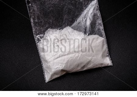 Cocaine in plastic packet on black background, macro closeup photo. Portion of drugs