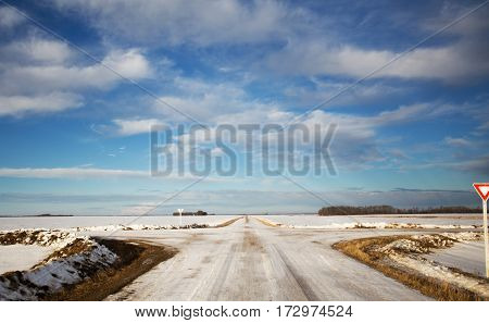Four way gravel roads disecting agriculture farmland dotted with forests of trees in a morning sunrise winter landscape
