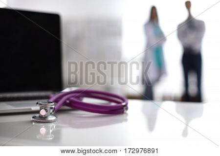 Laptop and stethoscope on the desk doctors standing in the background.