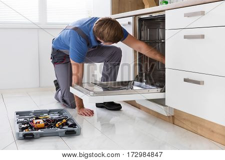 Repairman Examining Dishwasher With Toolbox In Kitchen