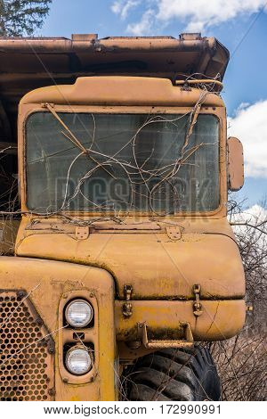 Rusting and overgrown heavy yellow industrial truck and equipment abandoned in economic recession