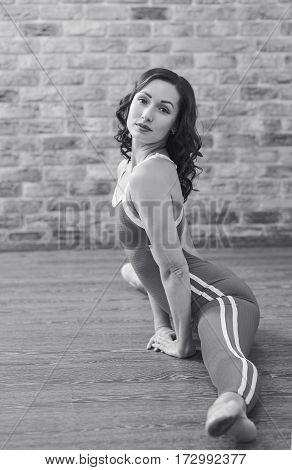 Full length portrait of young cuacasian ballet dancer practicing indoors. Sporty woman warming up and stretching at fitness class