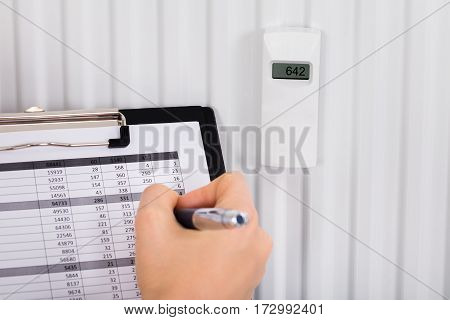 Person Hand Maintaining Records Of Digital Thermostat On Clipboard At Home