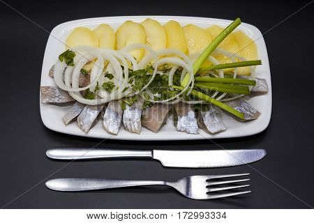 Tasty pieces of Icelandic herring with boiled potatoes and onions on the plate. National Icelandic snack Fat herring.