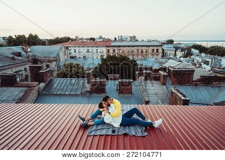Loving Young Couple Is Sitting On The Roof Of The House.