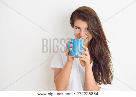 Young Brunette Woman In White T-shirt Drinking From Blue Mug With Both Hands, Looking At Camera With