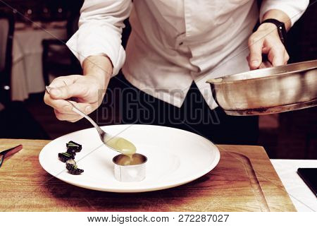 Chef is putting puree to plate using culinary form, toned image