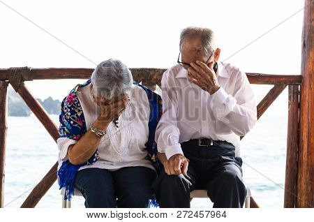Elderly Couple Looking At Each Other Laughing. Elderly Couple With The Sea Background.