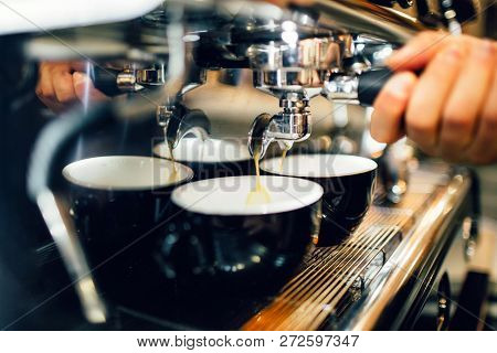 Close Up And Cut View Of Mans Hand Holding Cezve From Coffee Machine Above Two Cups. Coffee Is Pouri
