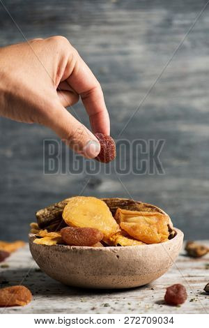closeup of a young caucasian man taking a dried strawberry from a rustic earthenware bowl full of an assortment of dried fruit, such as pear, peach, banana, strawberry, apple or apricot