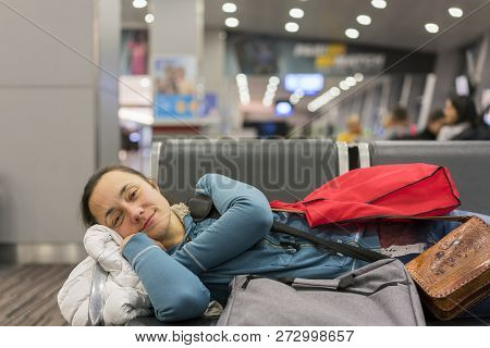 Young Woman Sleeping At The Airport While Waiting For Her Flight. Tired Female Traveler Sleeping On 