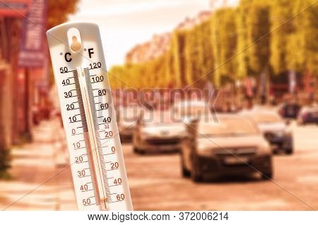 Thermometer in front of cars and traffic during heatwave.