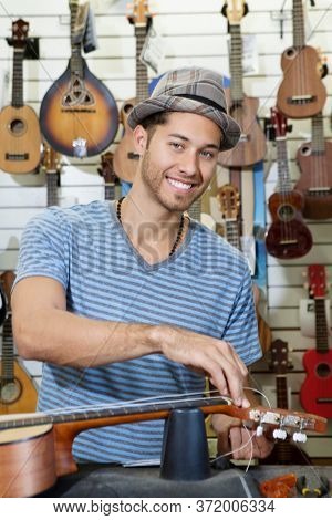 Portrait of a happy owner of music store restringing guitar