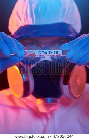 COVID-19 or 2019-nCoV. Close-up portrait of a scientist microbiologist in a protective PPE suit showing the coronavirus test tube. Vaccination.
