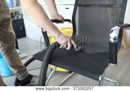 Close-up Of Person Cleaning Black Comfy Chair Using Compact Vacuum Cleaner. Place For Sitting. Man C