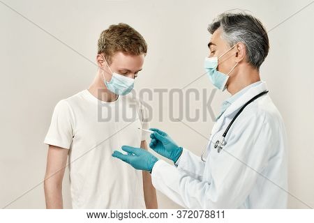 Body Temperature. Doctor In Uniform And Blue Sterile Gloves Measuring Temperature Of Young Male Pati