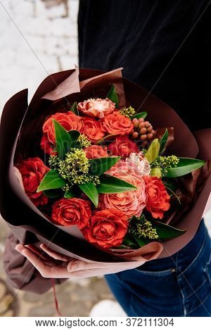 Bouquet Of Flowers In Burgundy Package In The Hands Of A Woman Florist On Background A White Brick W
