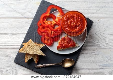 Ajvar Or Pindjur Red Vegetable Sauce, Paprika Pepper On A Black Board And Wooden Table. Serbian Trad