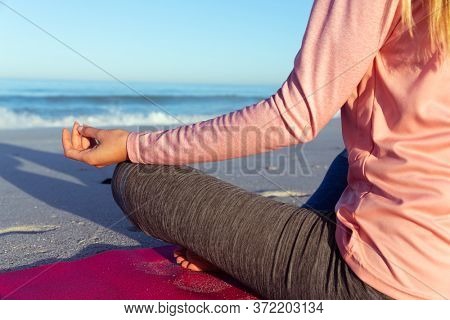 Mid section view of a Caucasian woman wearing sports clothes, enjoying time at the beach on a sunny day, practicing yoga, meditating in lotus position