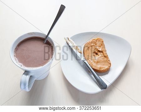 Top View Of Cup With Cocoa And Toast With Peanut Butter On Plate On Table