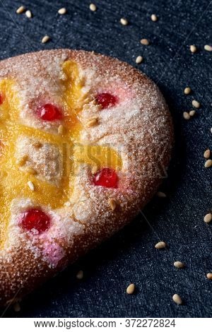 closeup of a coca de Sant Joan, a typical sweet flat cake from Catalonia, Spain, eaten on Saint Johns Eve, on a black fabric surface sprinkled with pine nuts