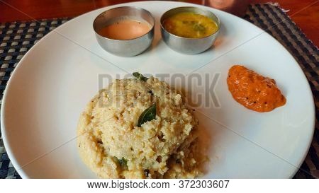 South Indian Rice Dish Pongal Served In A White Ceramic Plate, Along With Chutney And Sambar.
