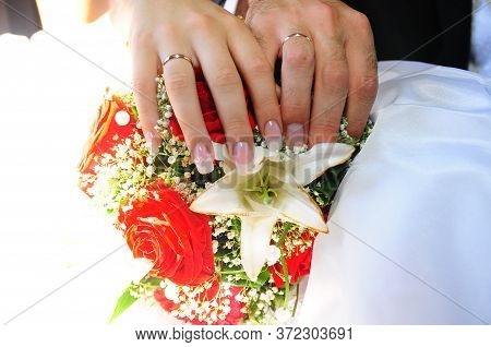 A Newly Weding Couple Place Their Hands On A Wedding Bouquet Showing Off Their Wedding Rings.