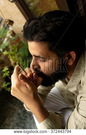 Top-down Shot Of A Bearded Indian Man Wearing Kurta Pyjama Smoking Weed Rolled In A Paper. He Is Tak