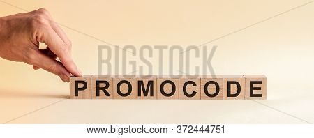 The Hand Puts A Wooden Cube With The Letter P From The Word Promocode. The Word Is Written On Wooden