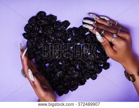 Woman Hands With Long Nails Manicure Holding Dry Fruits In Shape Of Heart On Purple Background