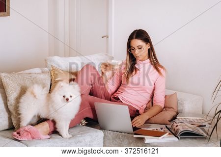 A Girl In Pajamas At Home Is Working On A Laptop With Her Dog Spitzer, The Dog And Its Owner Are Res