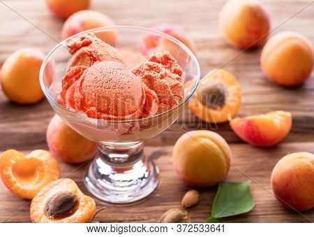 Homemade ice cream with apricot jam on the wooden table. Several apricots are near dessert bowl.