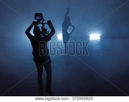 Professional videographer with gimball video slr recording video of female athletic dancer  while performing modern style ballet making acrobatic elements in a dark environment