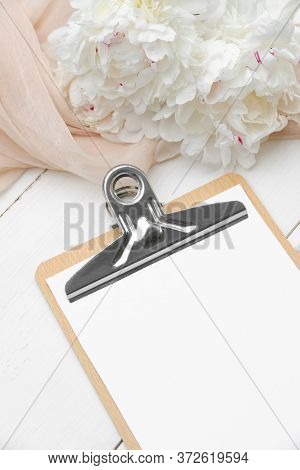 Close-up Clipboard With Blank Paper Mockup, Beige Cloth And Peonies On White Wooden Table. Wedding P