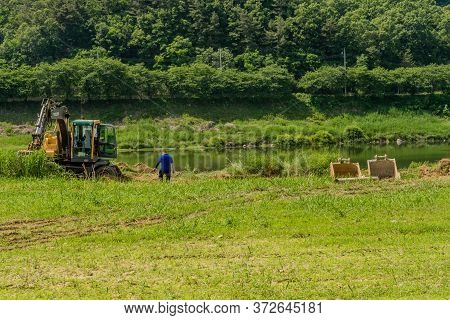 Cheongju, South Korea; May 31, 2020: Unidentified Man Walking Toward Backhoe Parked Beside River.